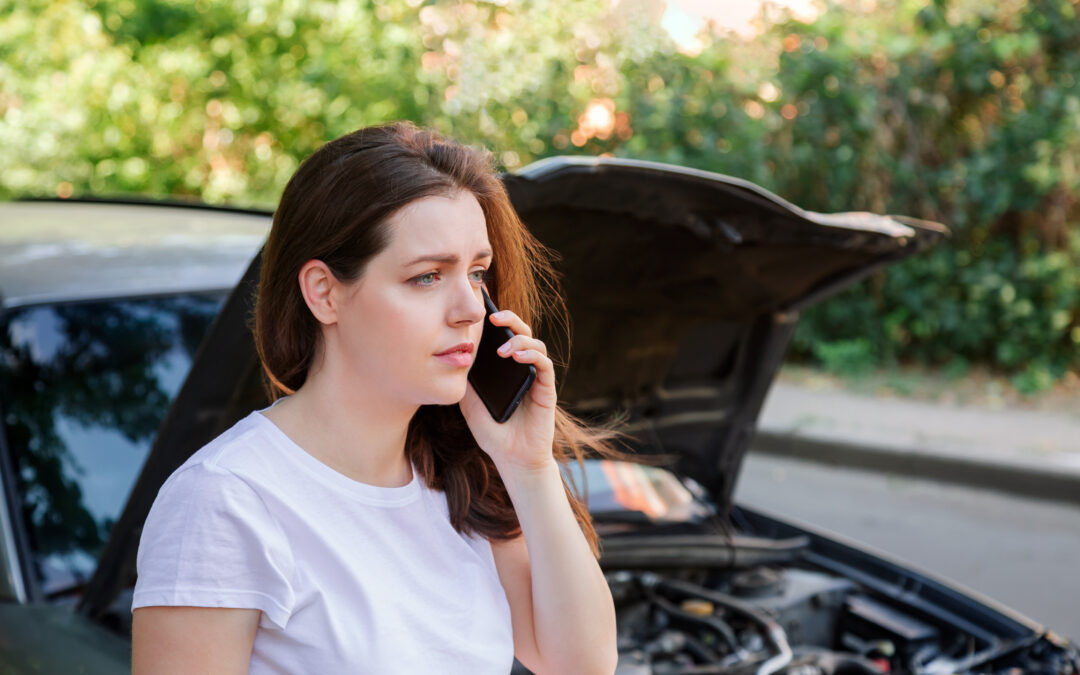 Woman in front of broken car with a mobile phone in hand